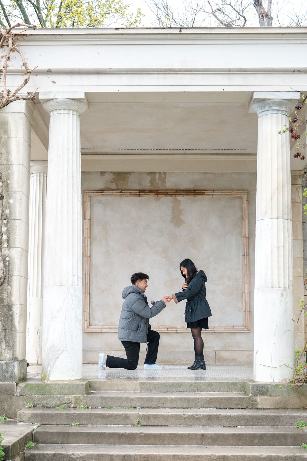 A romantic marriage proposal moment under a classical columned structure with stone steps at Untermyer Gardens in Westchester outside of NYC