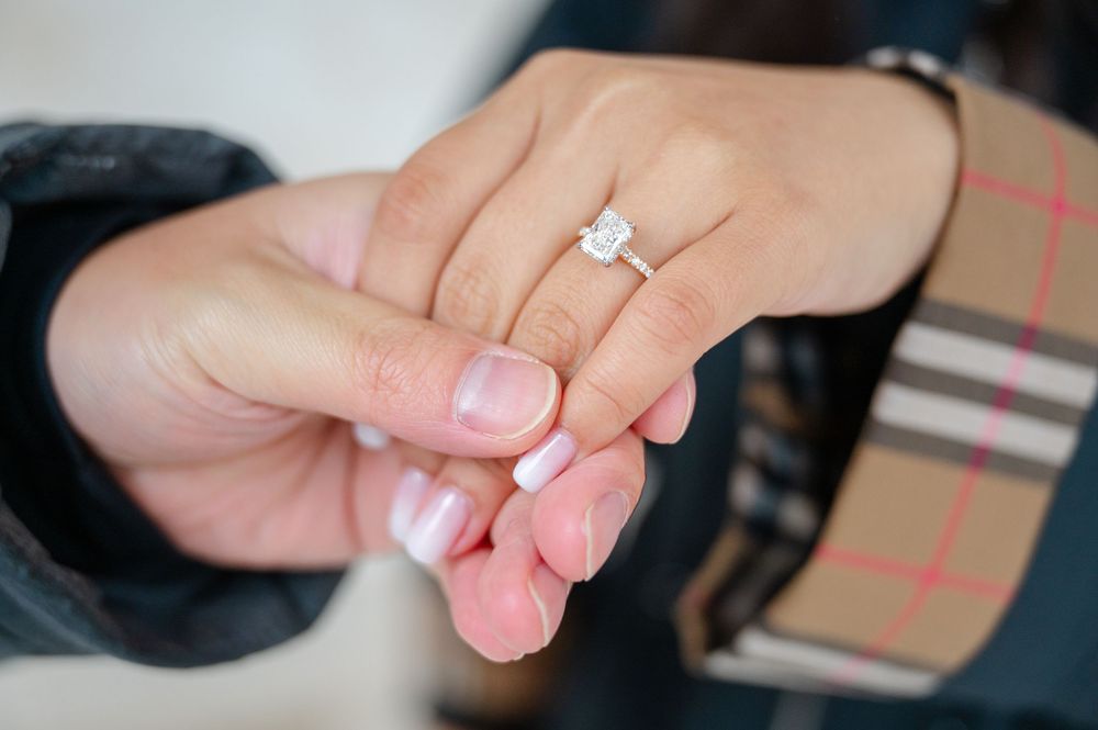 Close-up view of a delicate solitaire diamond engagement ring on a hand with pale pink manicured nails.