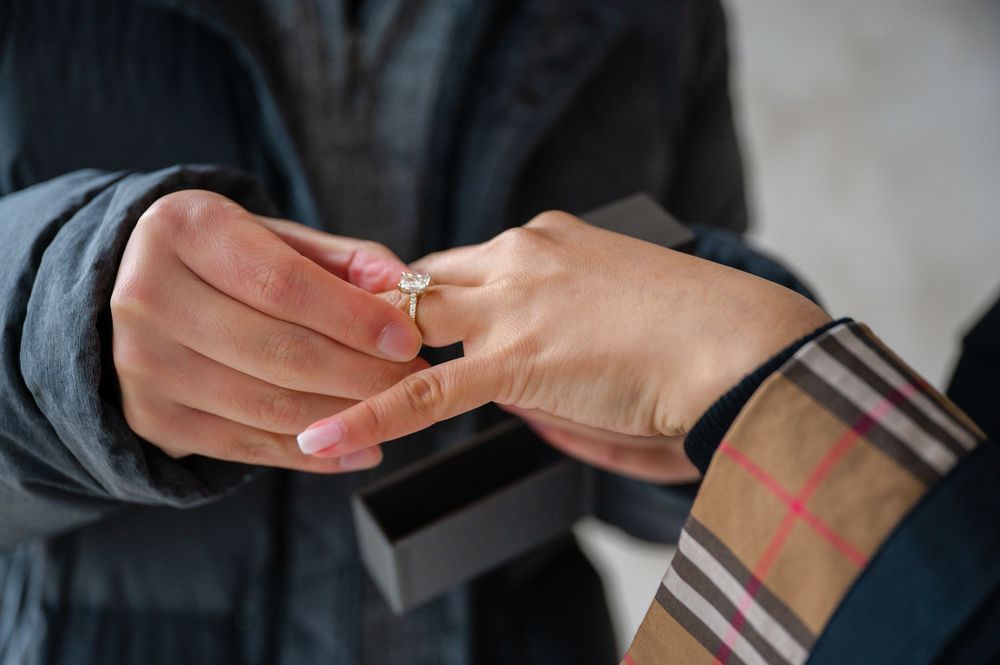 Close-up of hands wearing a plaid sleeve putting on a gold diamond engagement ring after proposal