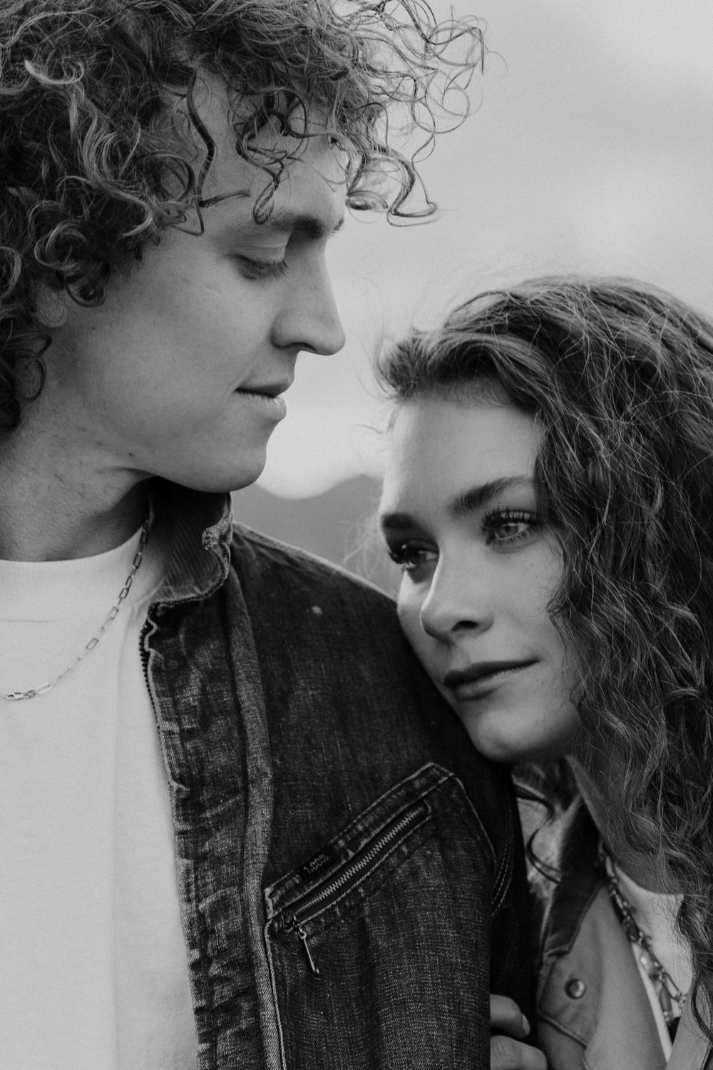 A romantic black and white portrait of a couple with curly hair gazing at each other intimately.