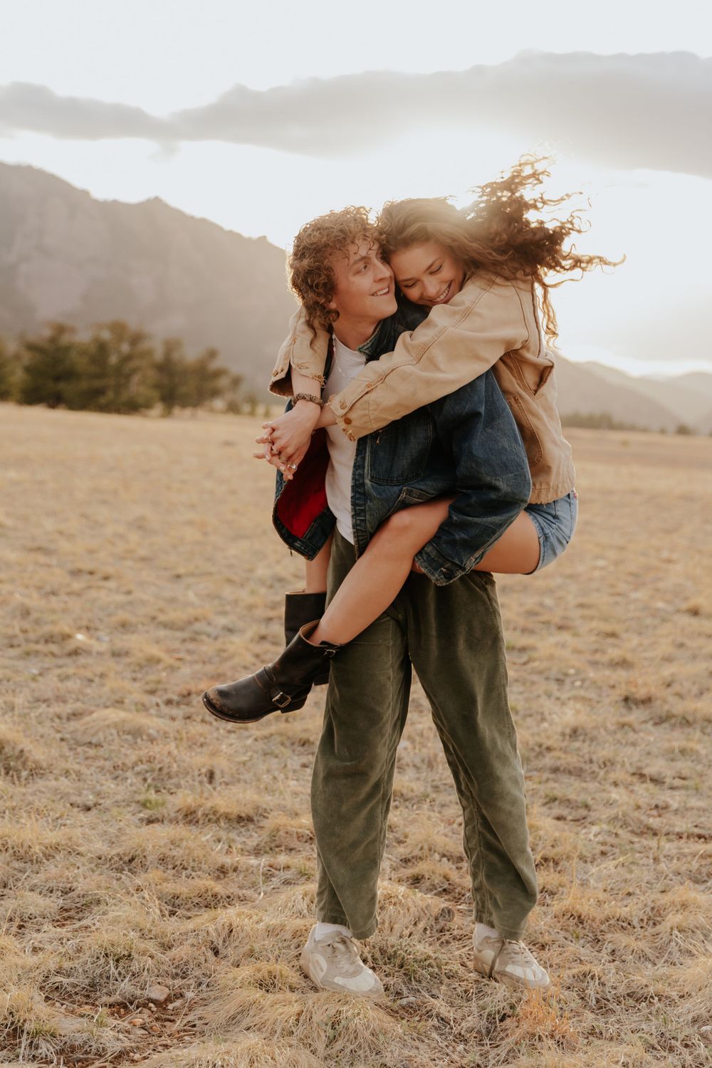 A playful piggyback ride moment captured in a golden field with mountains in the background at sunset.