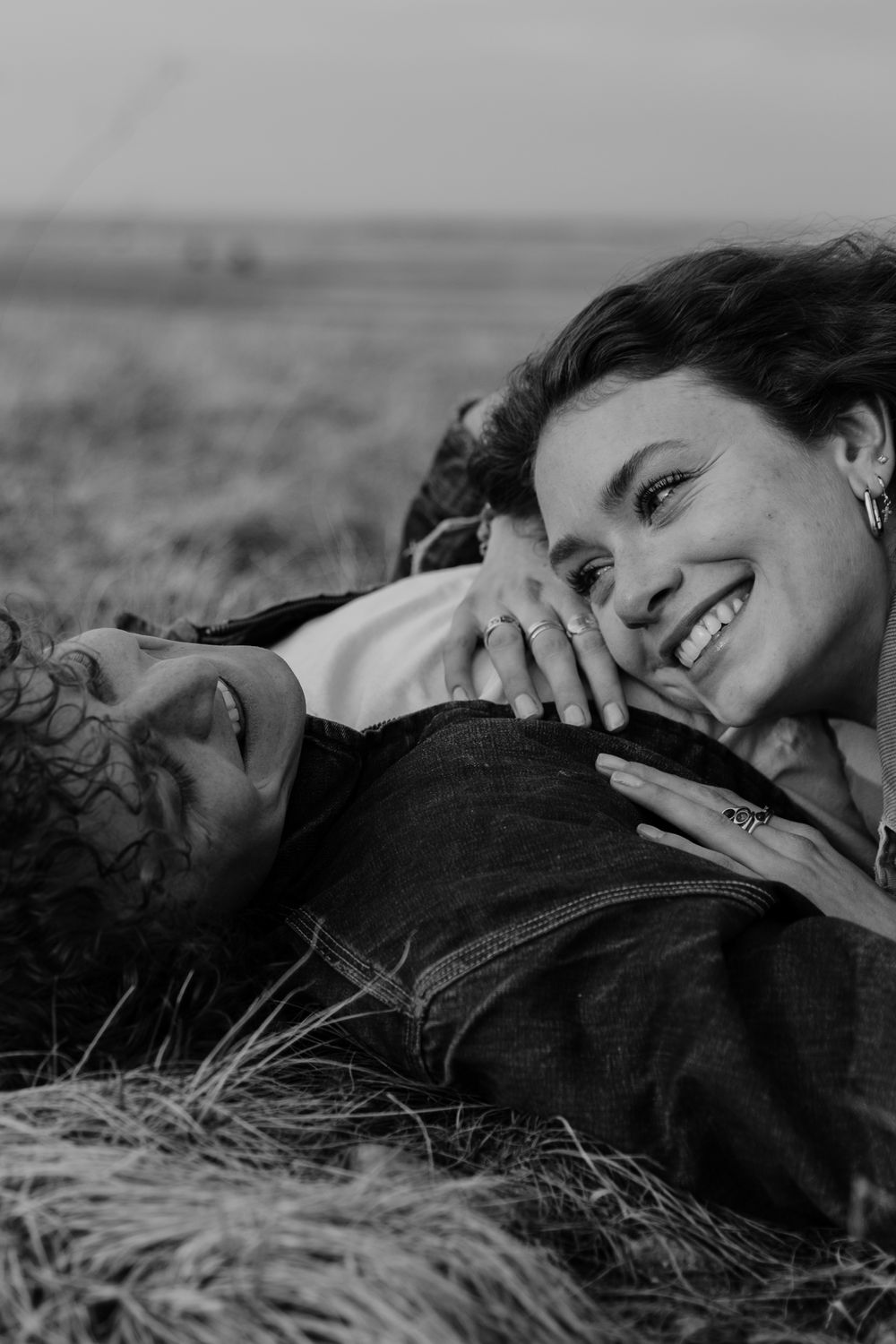 Black and white intimate portrait of a couple lying in grass and sharing a joyful moment together.