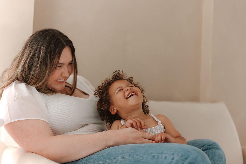 Two people share a joyful moment together while relaxing on a white couch, enjoying a tender interaction.