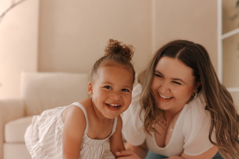 Two people share a joyful laugh while sitting together on the floor in a warmly lit room.
