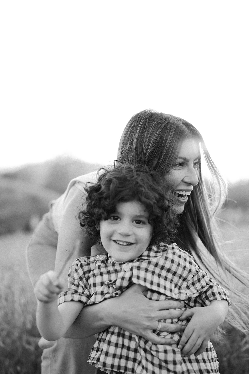 Black and white photo showing joyful moments in a field as two people embrace and laugh together outdoors.