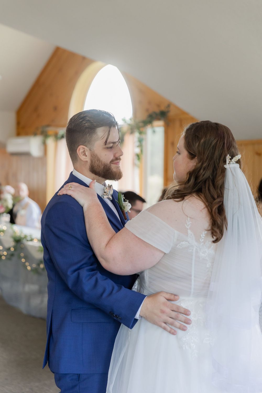 A couple shares their first dance in an elegant venue with arched windows and romantic lighting.