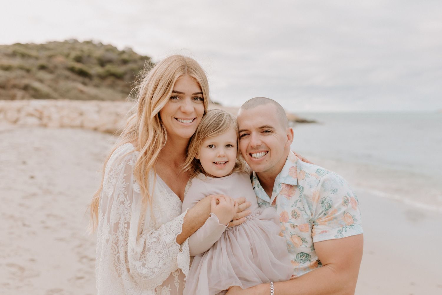 Happy family sharing a joyful moment together on a sunny beach with coastal dunes in the background.