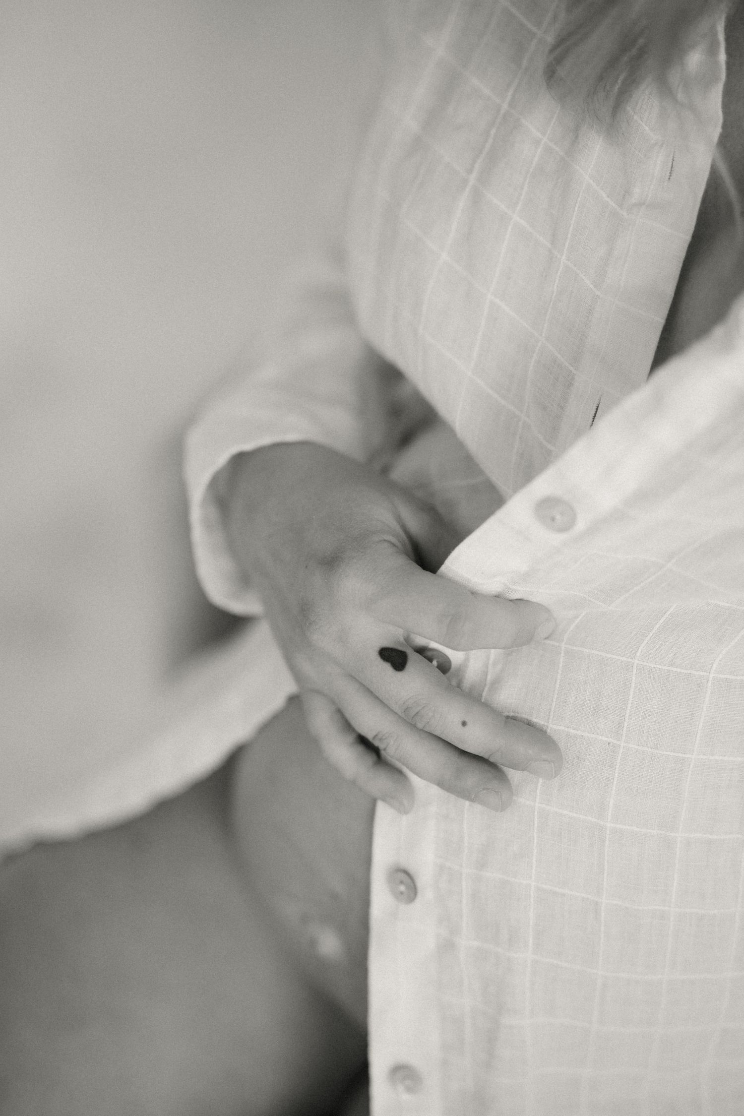 Black and white close-up of hands buttoning a white textured shirt.