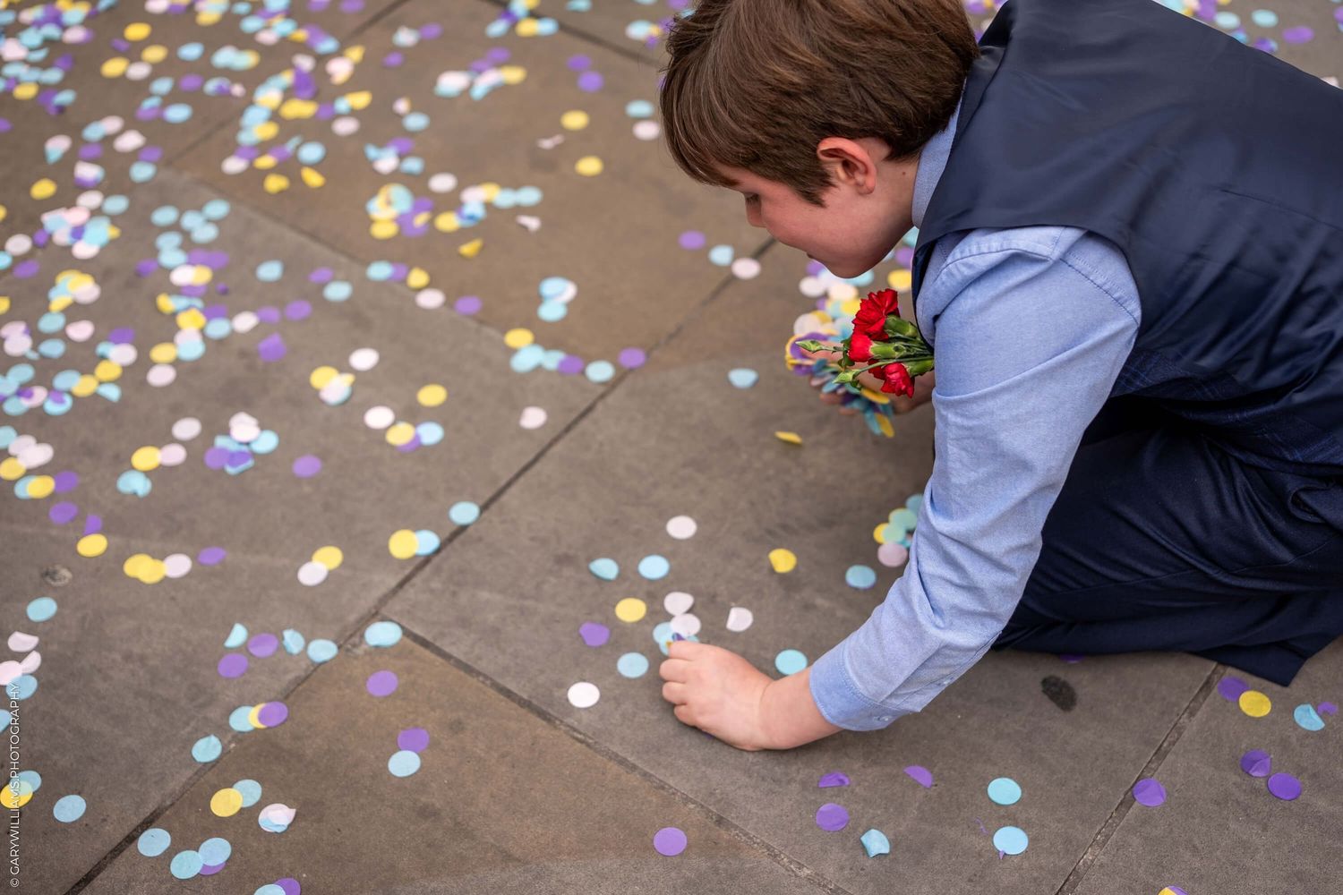 Person picking up colorful confetti scattered on a concrete ground at an event.