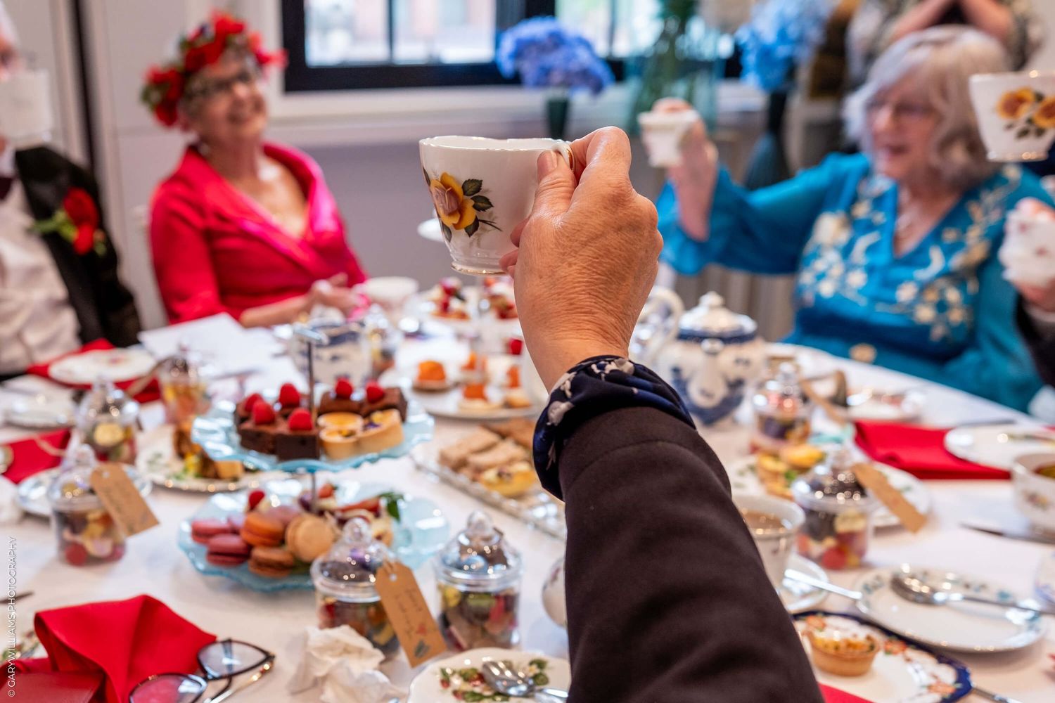 A hand raises a champagne glass during a festive holiday dinner party with a red and white decorated table setting.