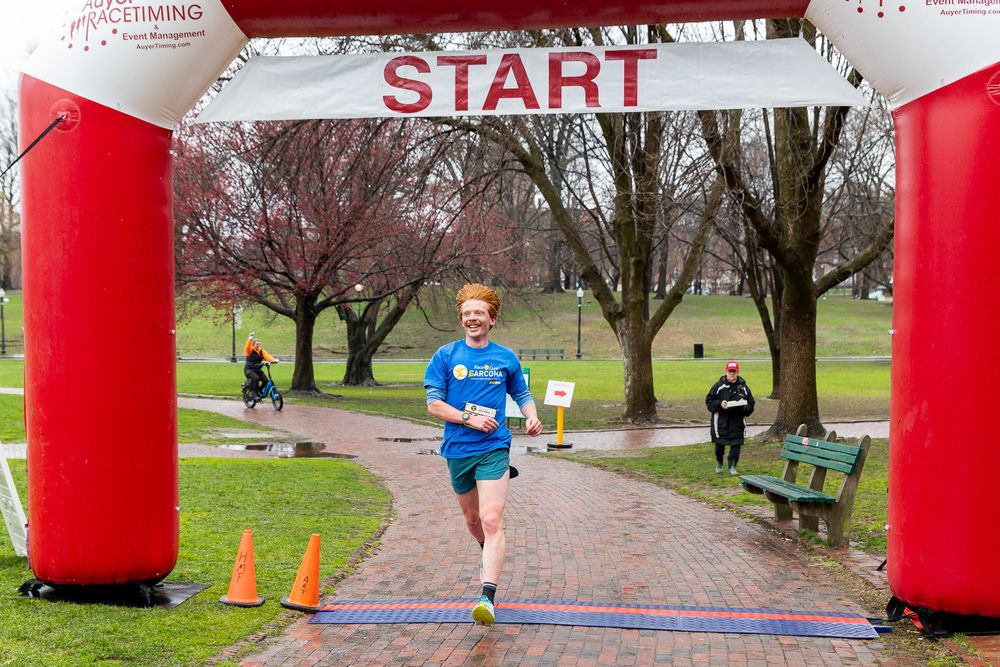 Marathon runner in blue shirt passing through red inflatable arch gateway during outdoor race in park setting.