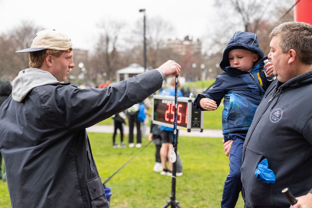 Runners get race bibs and instructions at a cold outdoor event on a grassy field.