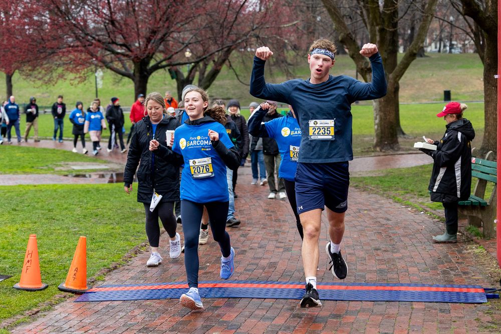 Runners crossing finish line at outdoor racing event on rainy winter day with orange cones marking path.