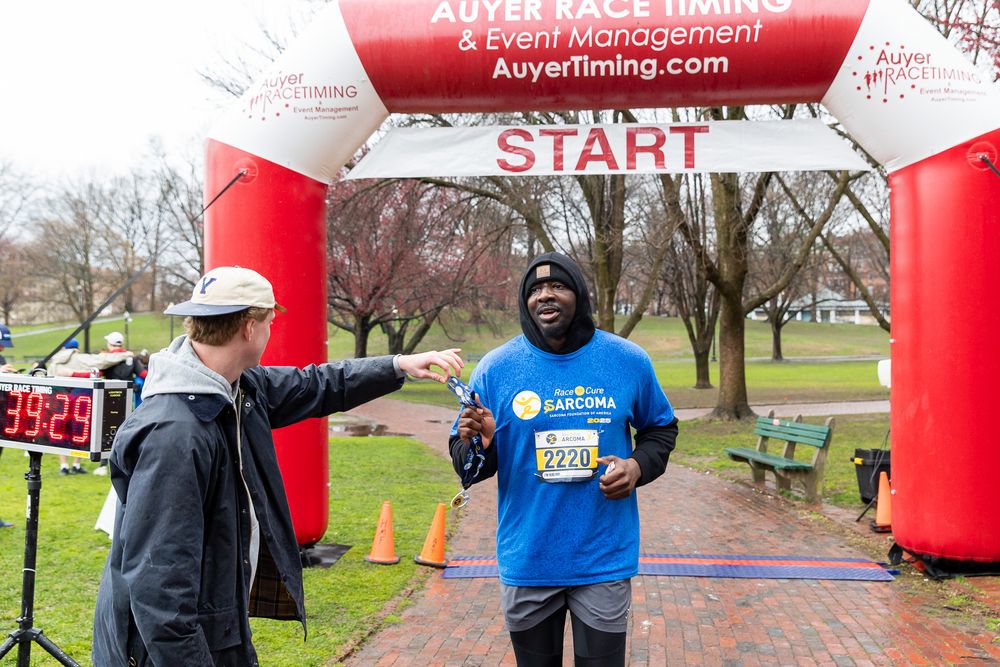 Runner celebrates at finish line under red inflatable arch during outdoor race event.