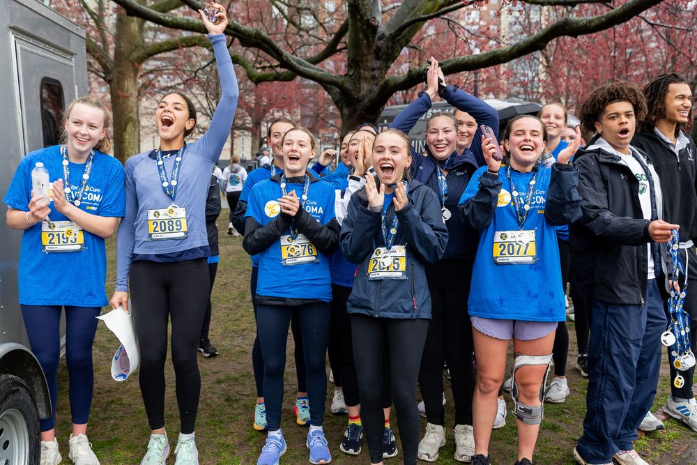 Group of runners in blue shirts celebrating together after a race with medals and race bibs.