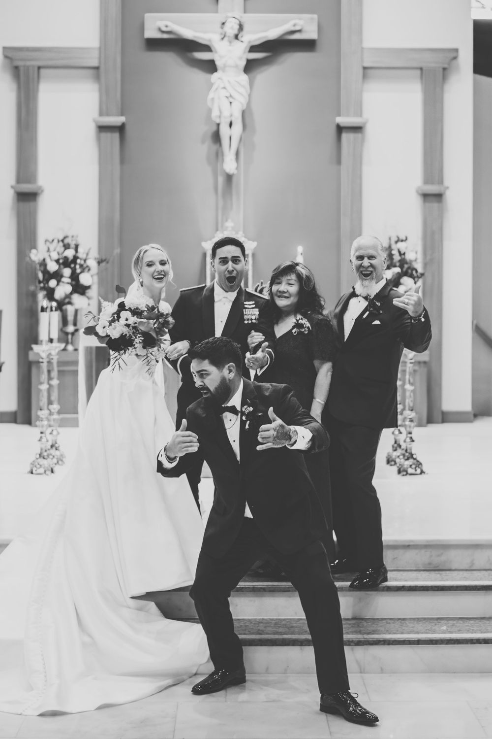 Black and white wedding photo showing joyful celebration in church with crucifix on wall and floral decorations.