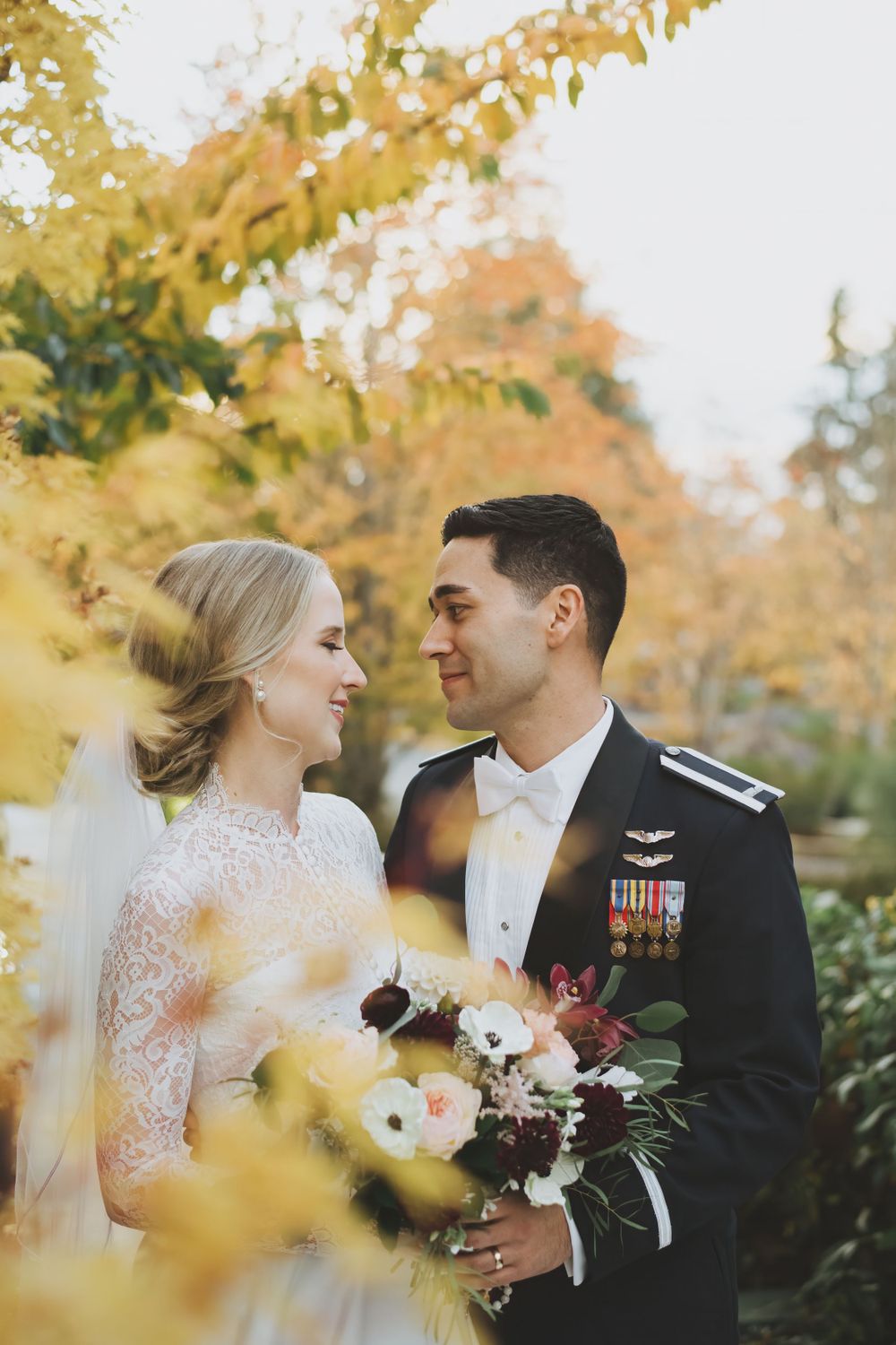 A romantic autumn wedding portrait with yellow foliage, white lace dress and military dress uniform with medals.