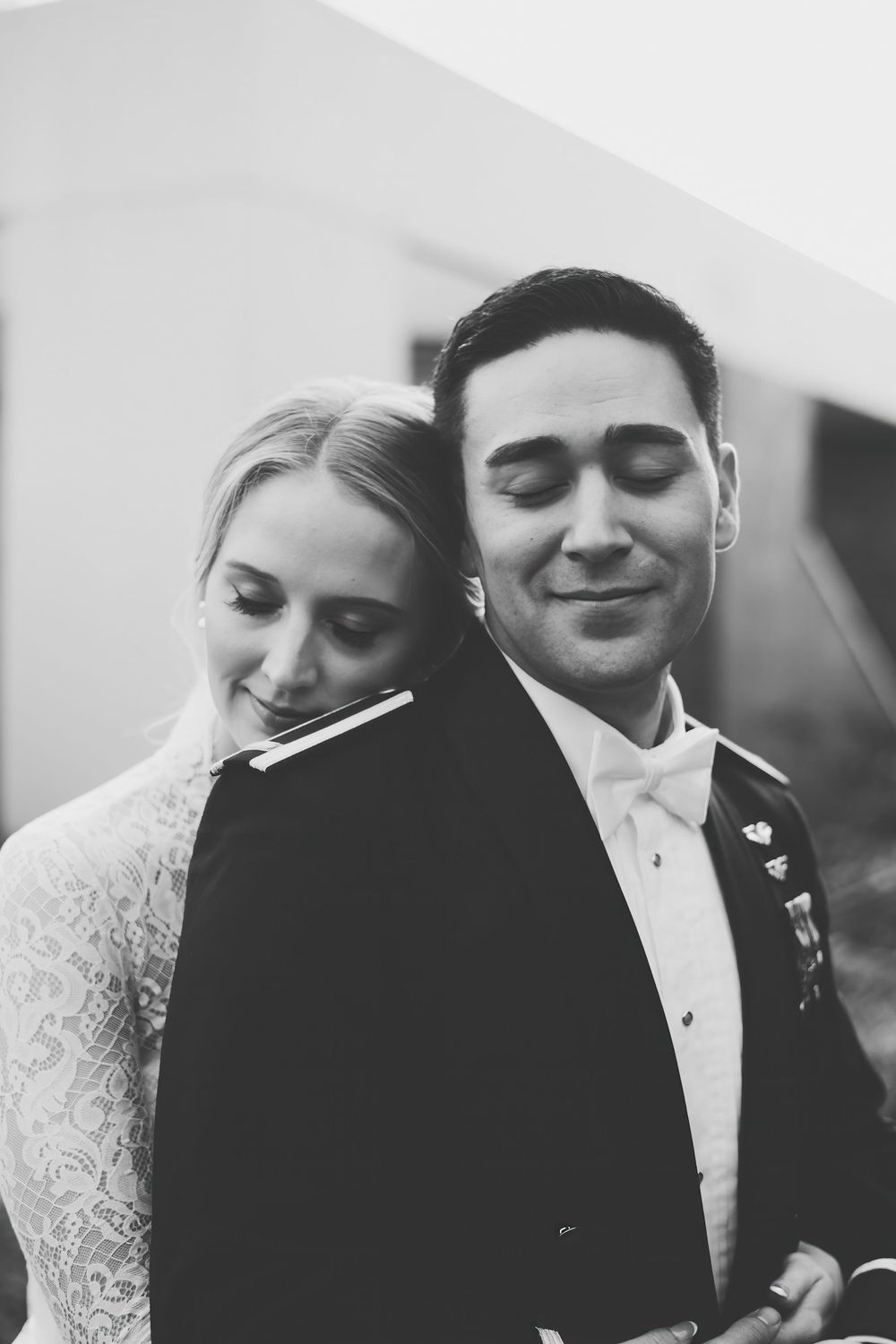 Black and white wedding portrait photo of a couple in formal attire smiling with eyes closed in an intimate moment.