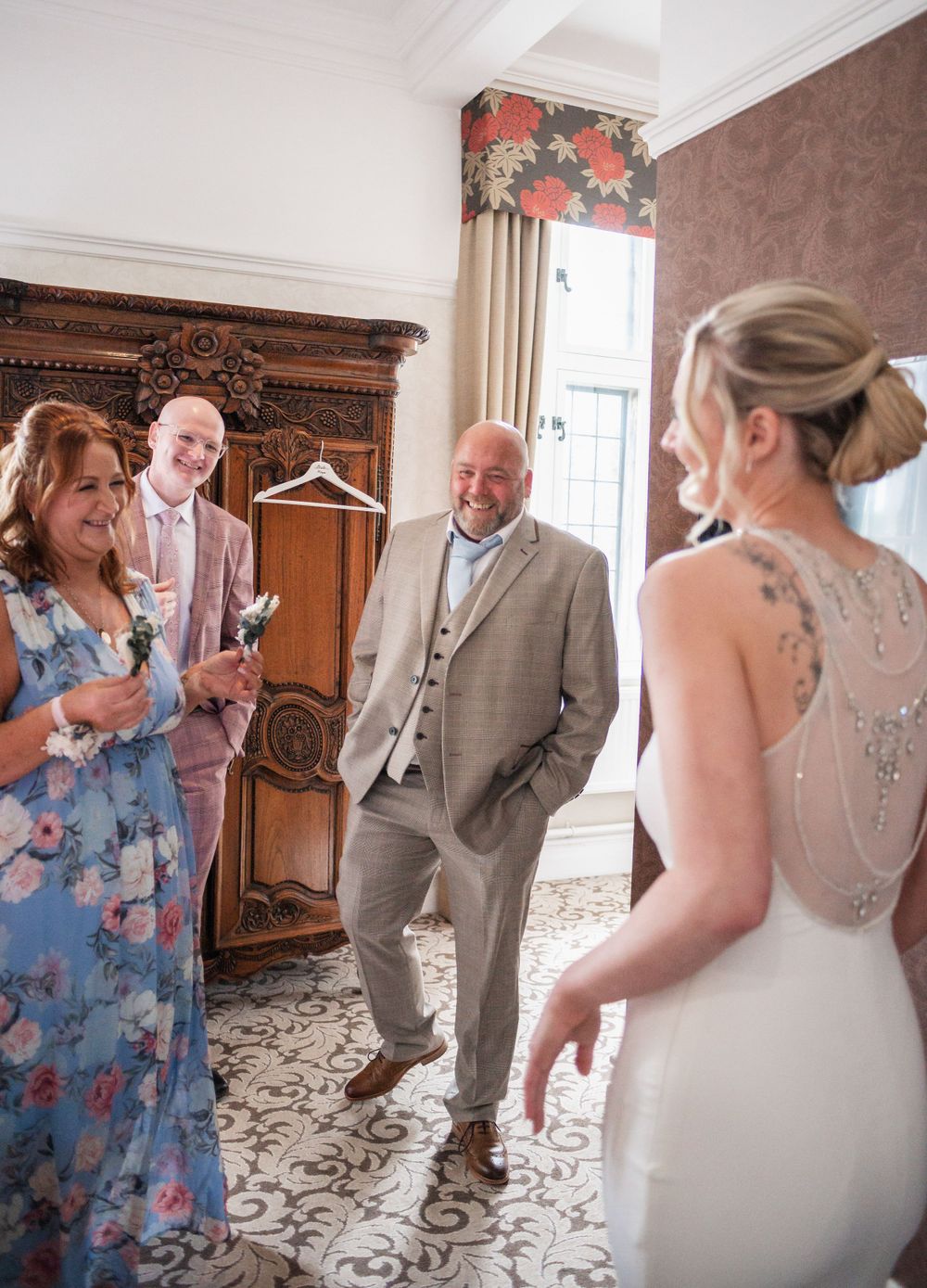 A bride in a lace-back dress greets wedding guests in an elegantly decorated room.