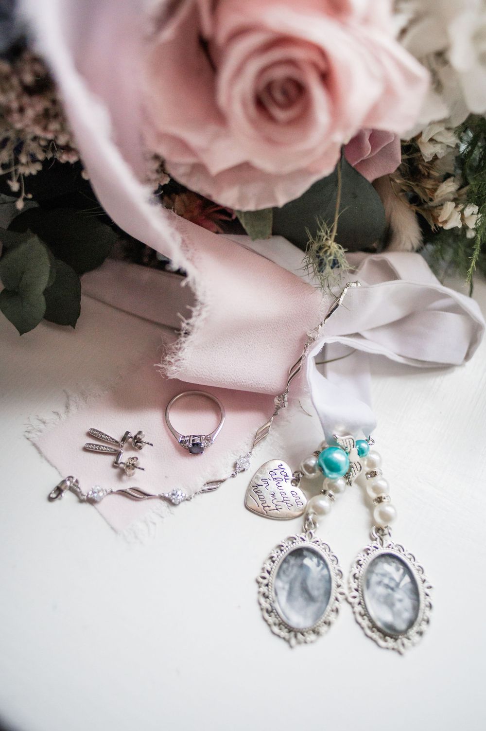 Wedding accessories including jewelry, rings, and vintage photo frames arranged with pink roses and ribbons.