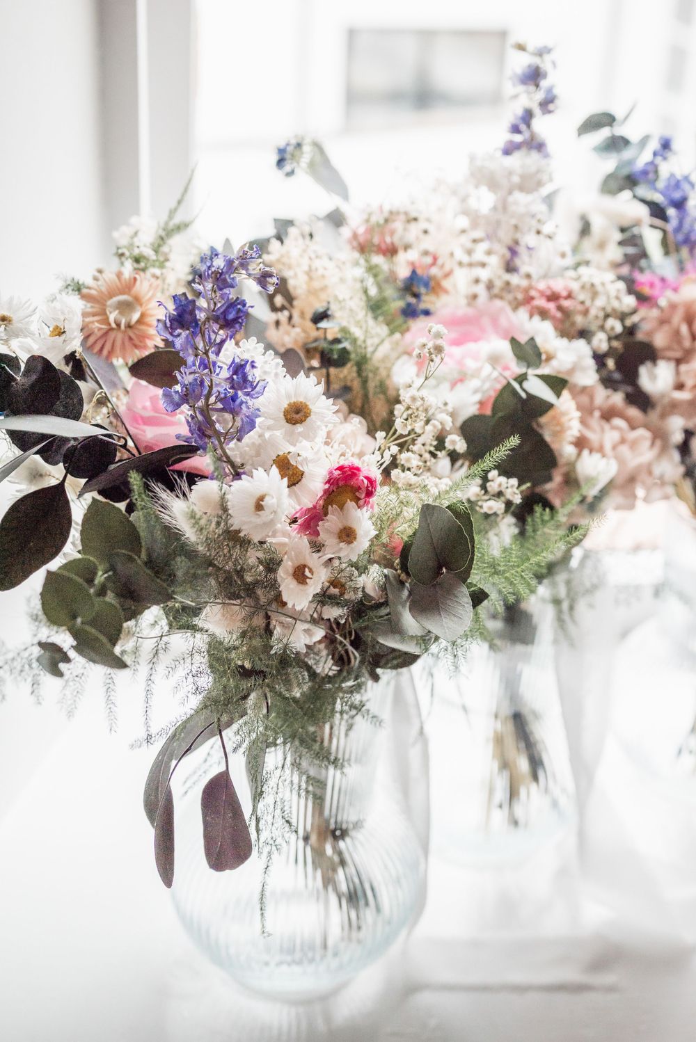 A soft and romantic floral arrangement with pink, purple, and white flowers in a clear glass vase.