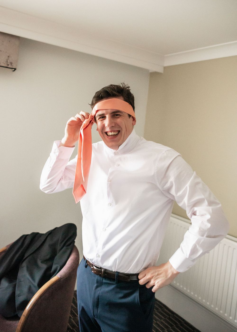 Getting ready moment showing preparation with coral tie and white dress shirt.