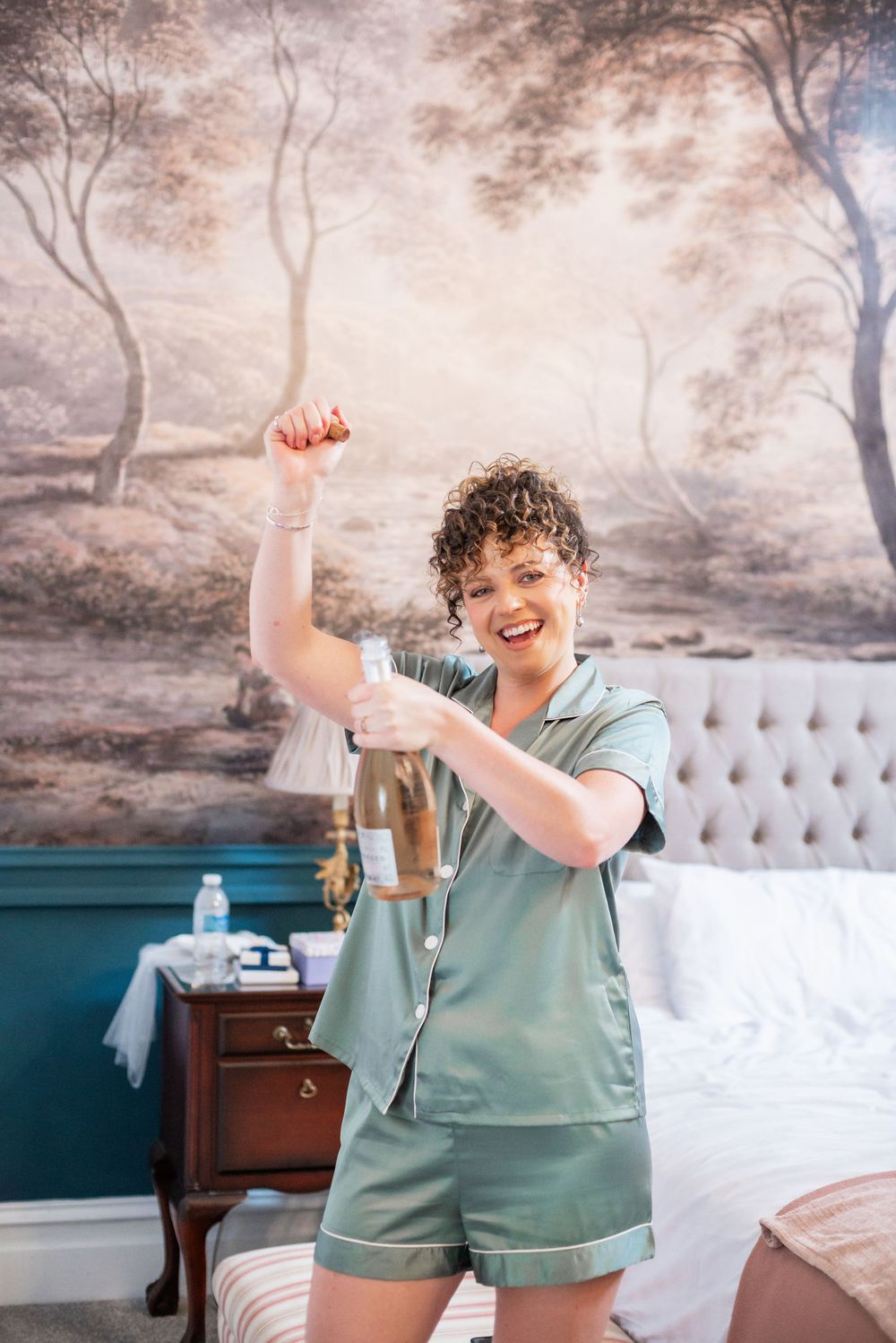 Person in mint green pajamas celebrates joyfully against painted forest wall mural.