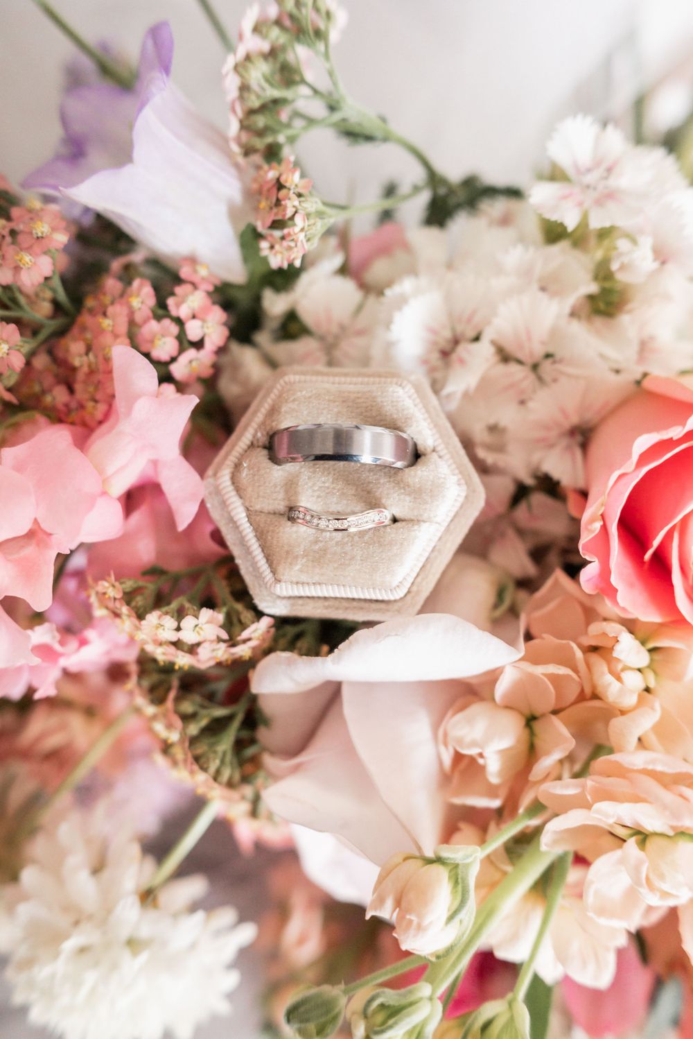 Wedding rings displayed in hexagonal box surrounded by pink and white flowers.