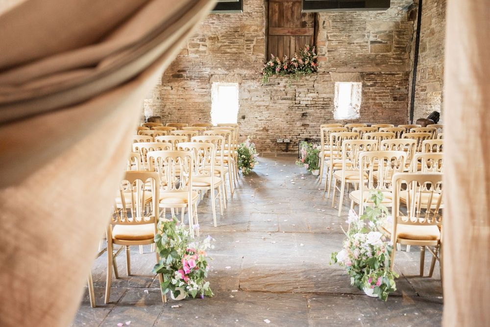 Rustic wedding ceremony setup with wooden chairs and floral aisle decorations in brick venue.