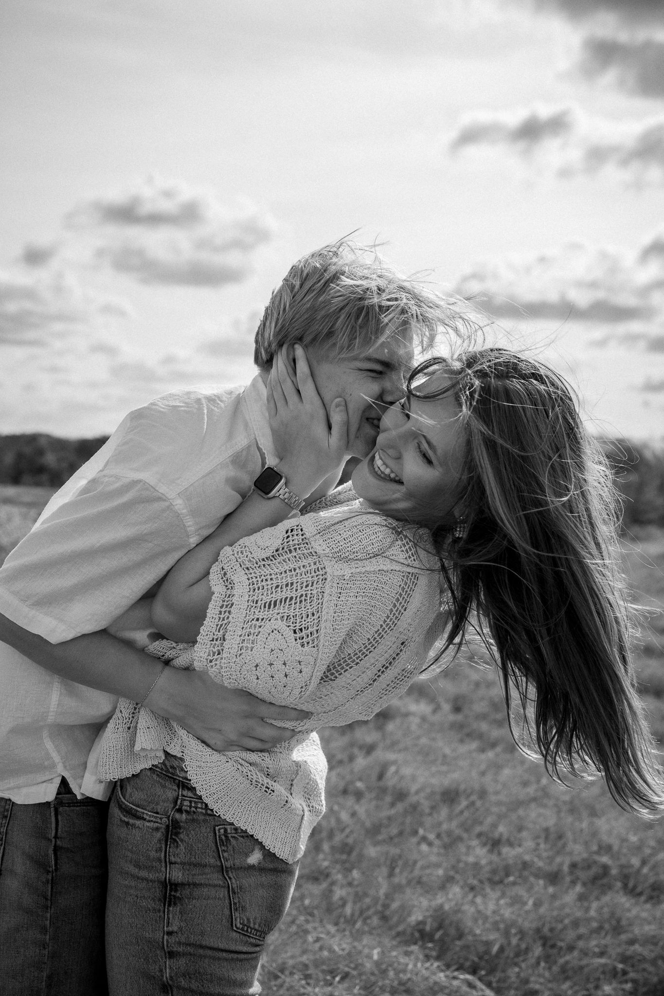 A romantic black and white photo of a couple embracing in a field at sunset.