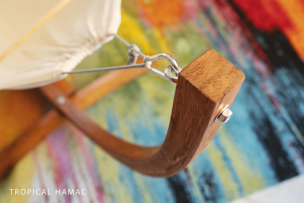 Close-up detail of a handcrafted wooden eyewear frame showing metal hinge attachment against colorful background.