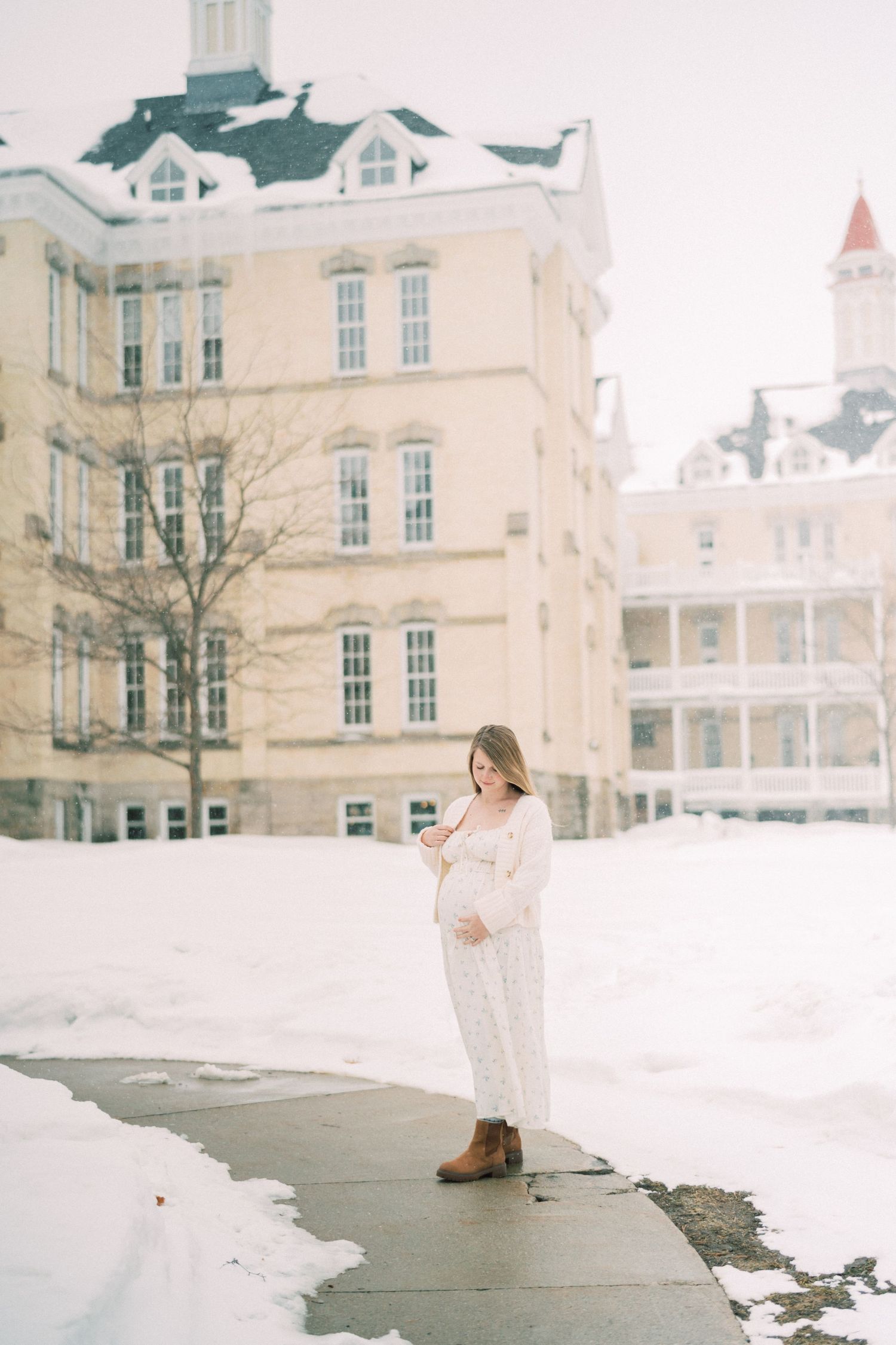 A person in a white winter dress stands on a snowy path outside a grand historic hotel building.
