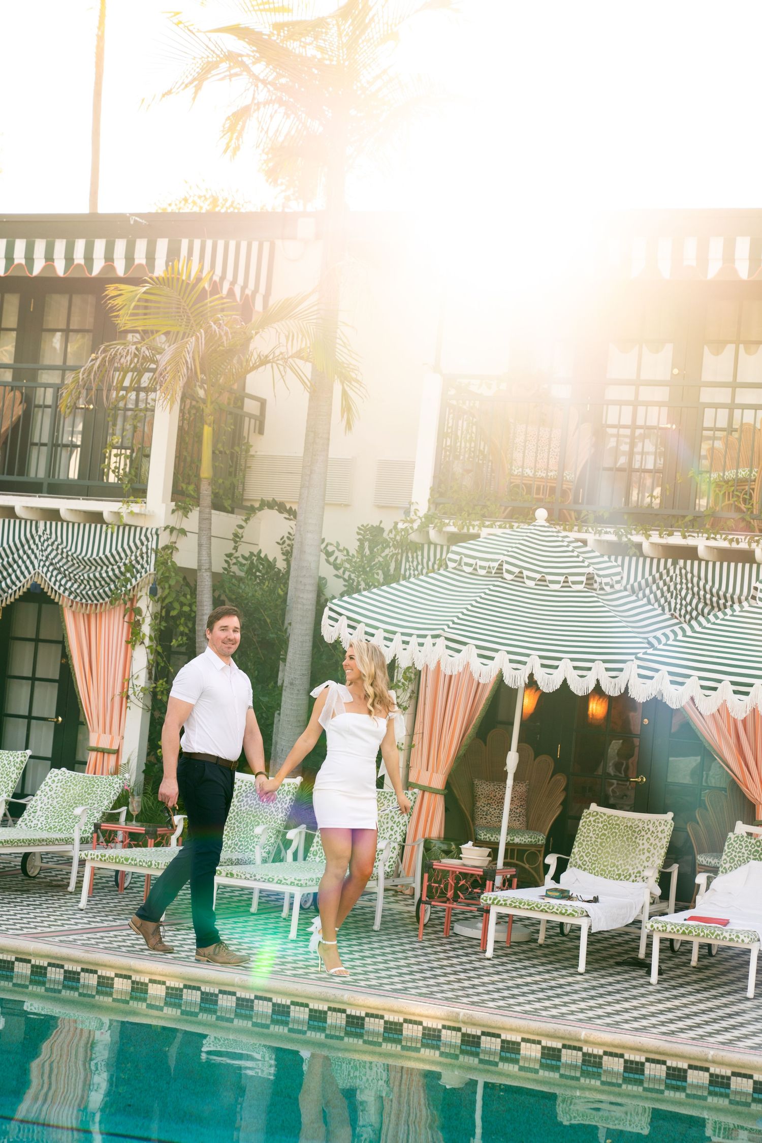 Sun-drenched portrait by resort pool with striped cabanas and palm trees. Engagement Session at The Lafayette Hotel in San Diego. Jessica.
