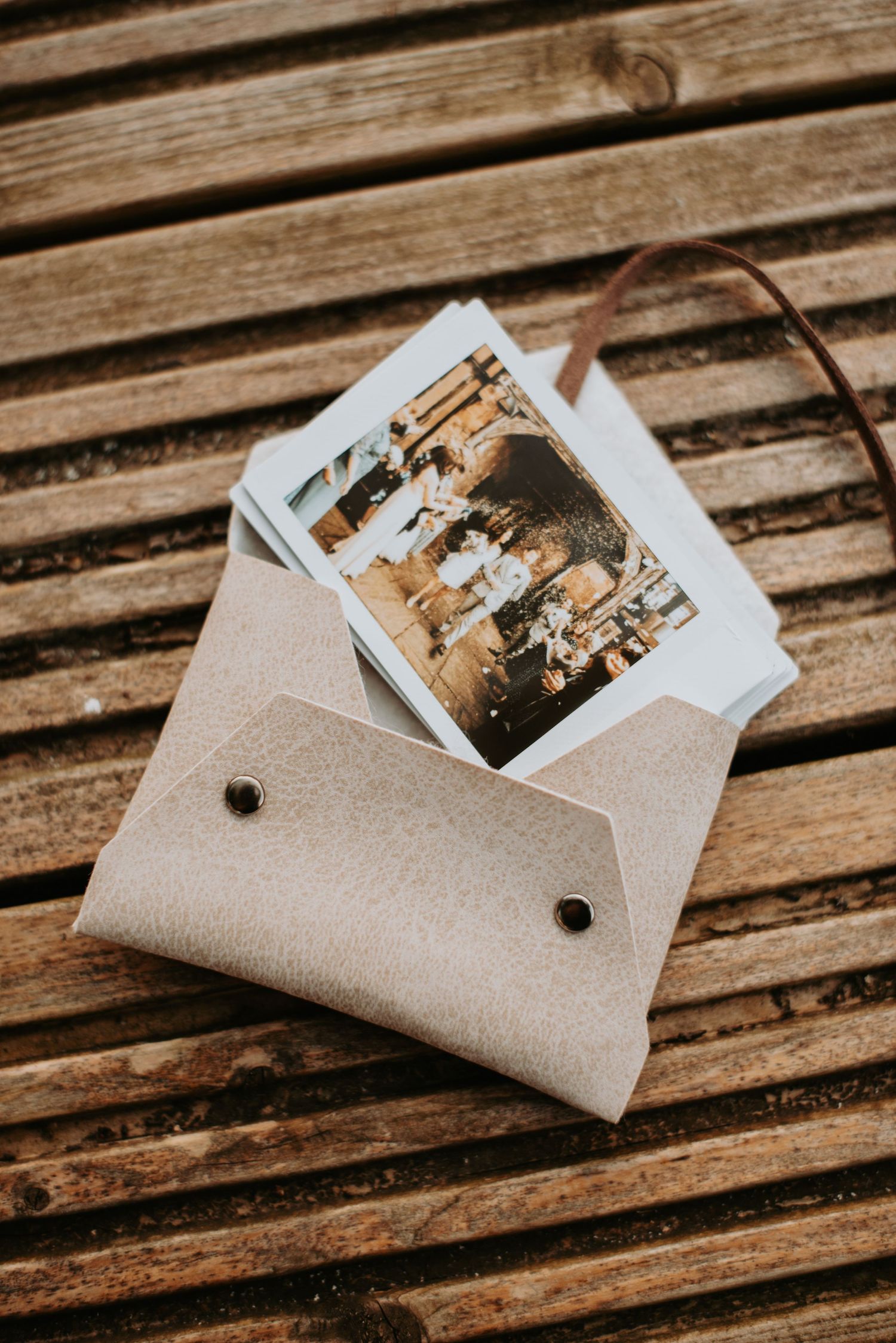 A vintage photograph in a small beige envelope rests on weathered wooden slats in warm lighting.