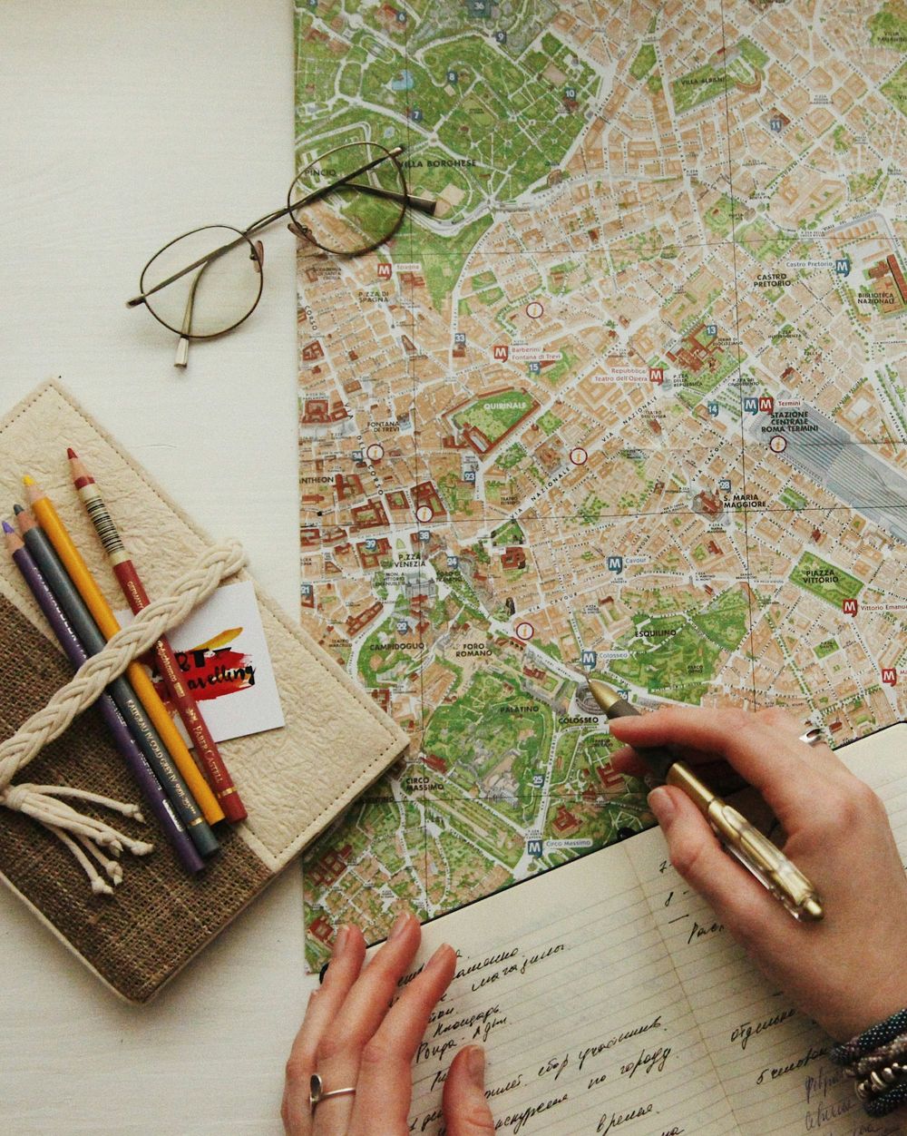 Overhead view of hands marking locations on a city map with glasses and pencils nearby.
