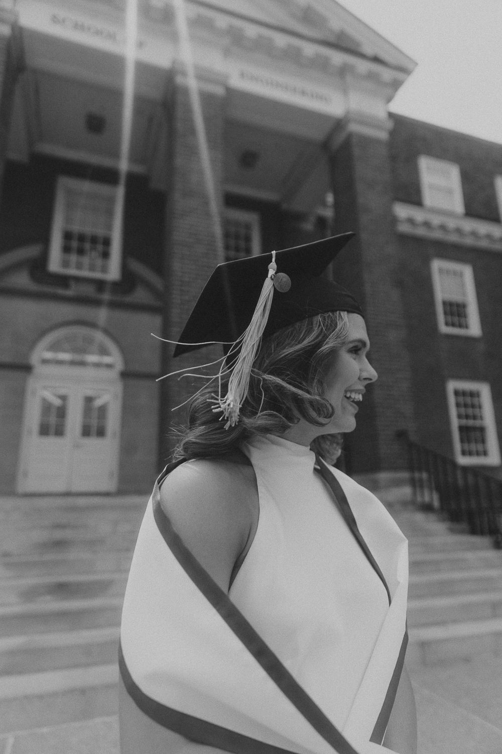 Graduation photo in black and white showing a graduate in cap and gown smiling in front of a classical building.