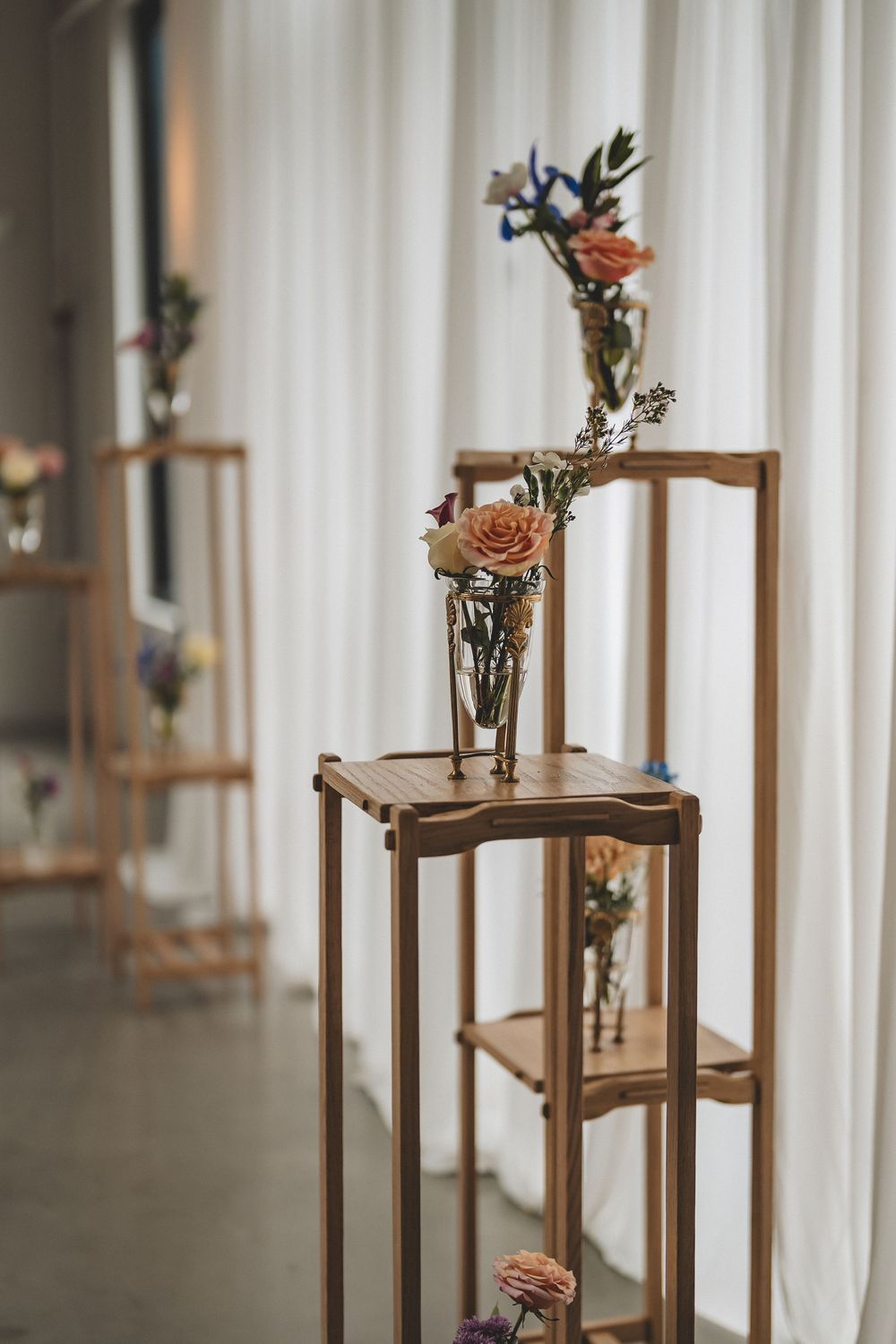 Wooden pedestals displaying delicate floral arrangements with peach roses against a white curtain backdrop.