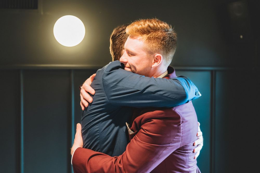 Two people sharing an emotional embrace under a bright glowing light in an indoor setting.