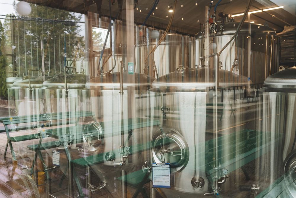 Large stainless steel brewing tanks visible through glass windows in a modern brewery facility.