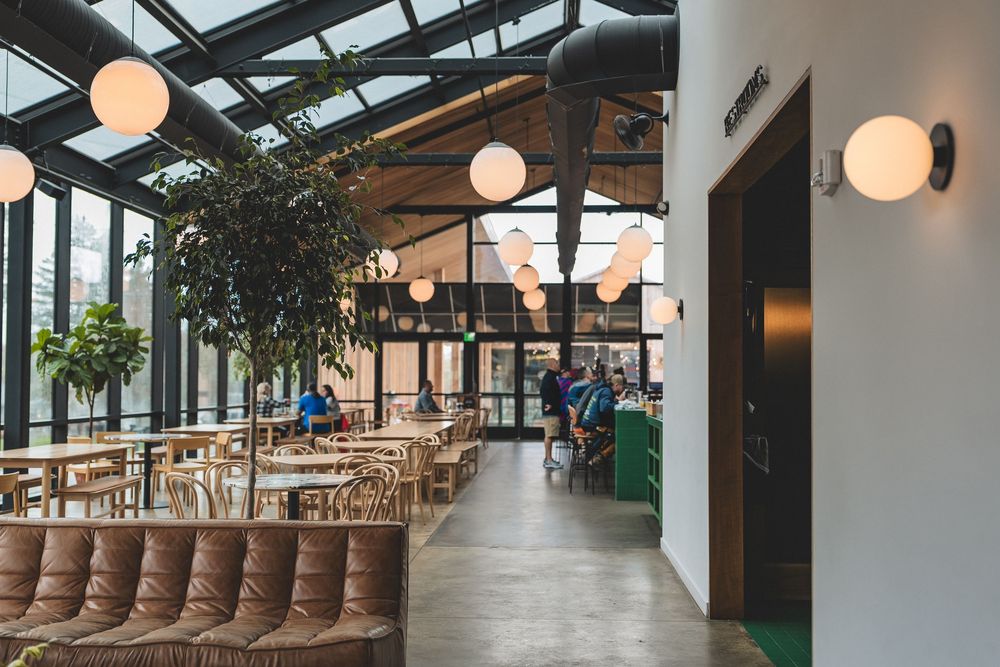 Modern restaurant interior with globe pendant lights and wooden furniture under a glass ceiling.