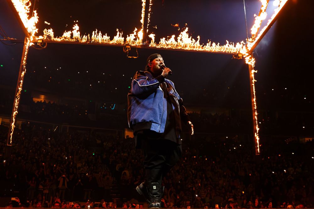 A dramatic concert performance by country rock artist Jelly Roll with flaming pyrotechnics creating fiery arches on stage at Bridgestone.