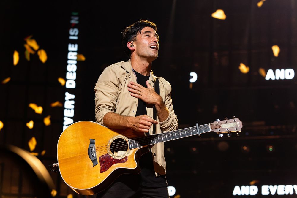 Christian artist Phil Wickham performing on stage with acoustic guitar under dramatic concert lighting at Bridgestone Arena.