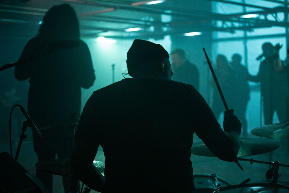 Silhouetted drummer and band members performing in moody blue-green stage lighting for a Cross Point Music video shoot.