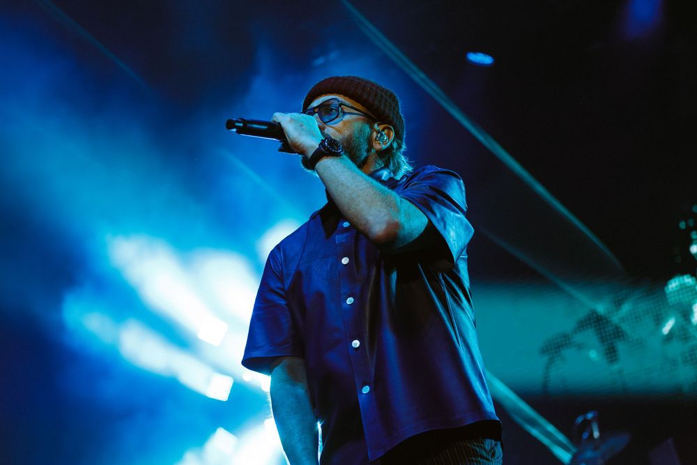 Christian Music artist Toby Mac in casual attire singing passionately against vibrant blue stage lighting at Bridgestone Arena in Nashville.