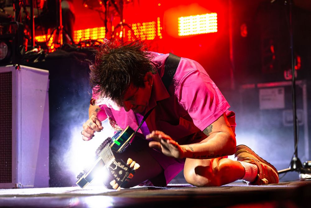 Performer Judah and the Lion in pink outfit crouching dramatically on stage under intense red concert lighting at Bridgestone Arena.