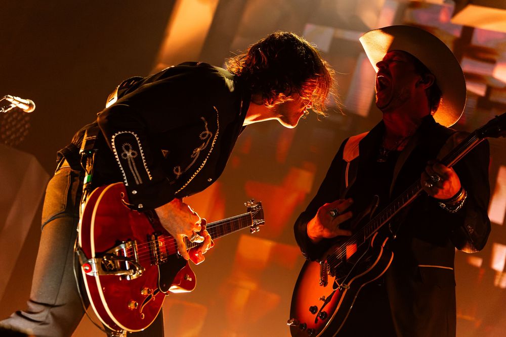 Two guitarists in Need to Breathe performing together on stage illuminated by warm orange concert lighting at Bridgestone Arena.