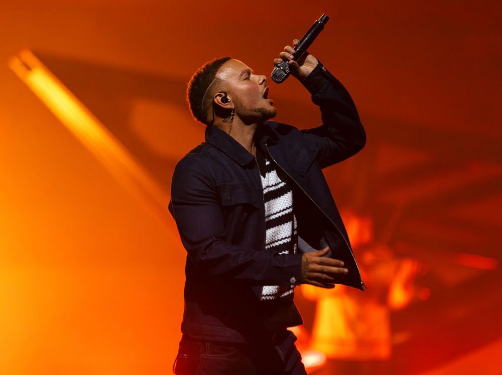 Country performer Kane Brown sings passionately against a dramatic orange-lit backdrop during a concert performance at Bridgestone Arena.