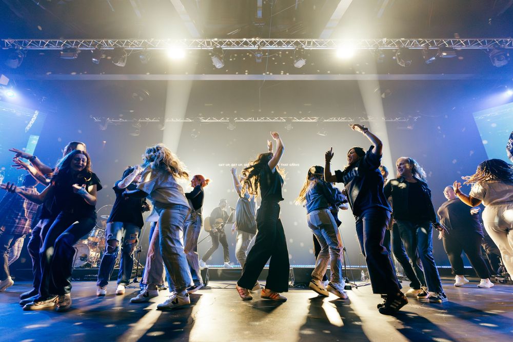 Silhouetted crowd of worship leaders dancing together on illuminated church stage.