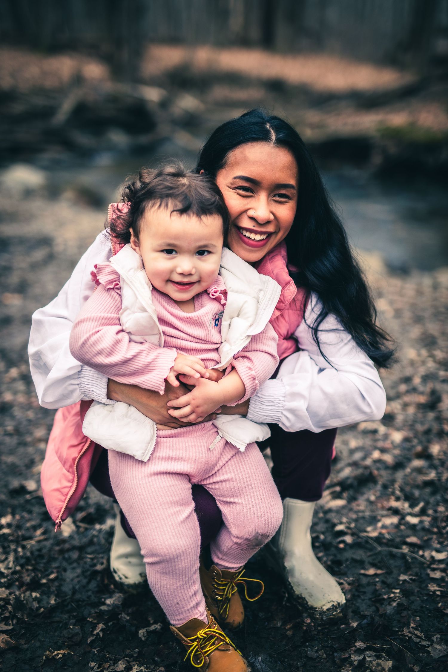 Two people in pink outfits sharing a joyful moment together outdoors on a wooded path.