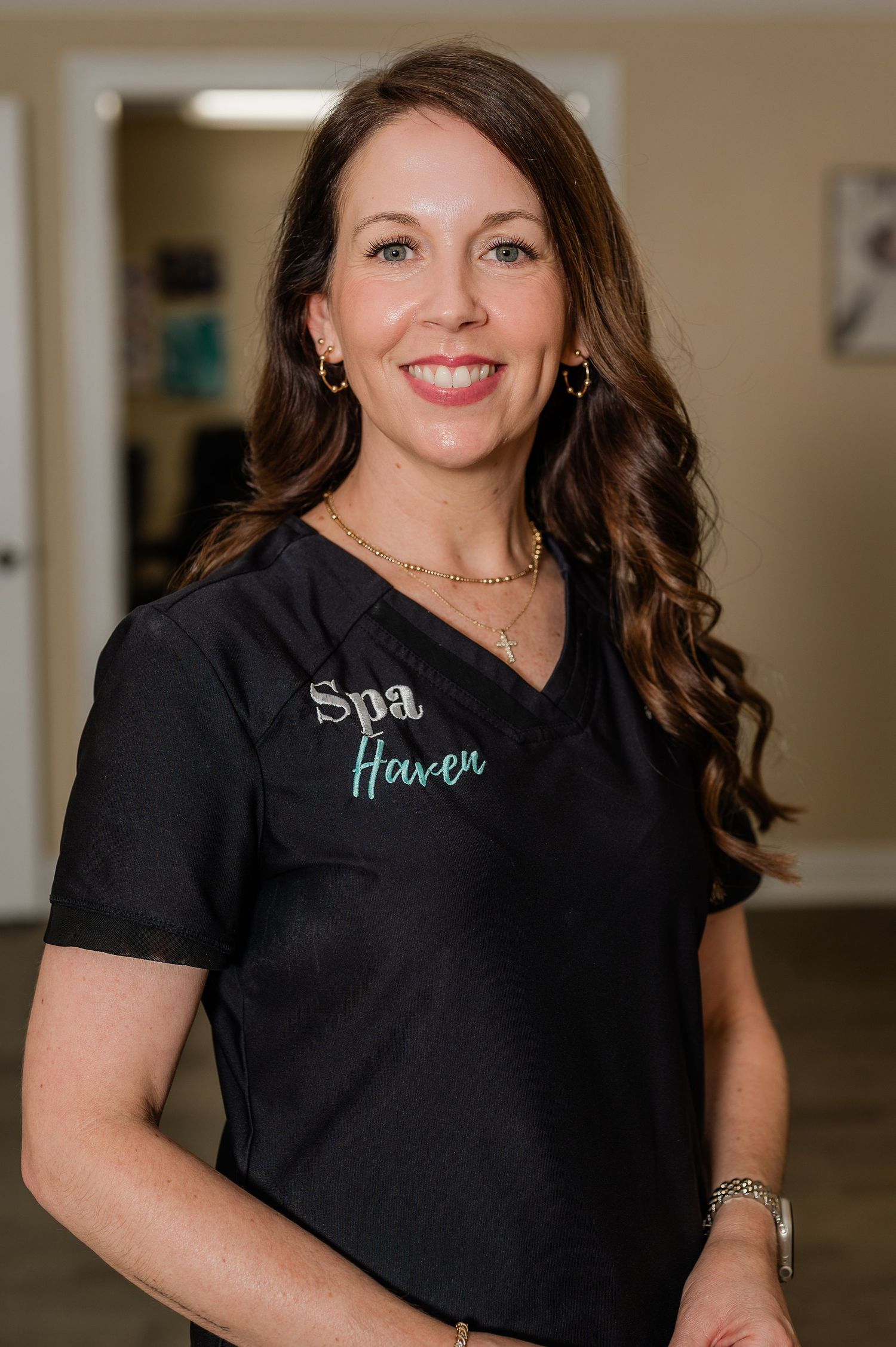 A spa professional wearing a black uniform with 'Spa Haven' embroidery stands in an office setting.